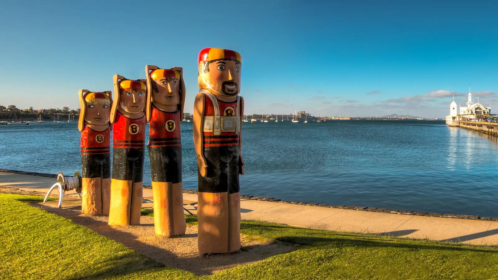 Painted timber bollard figures on the Geelong waterfront beside Corio Bay