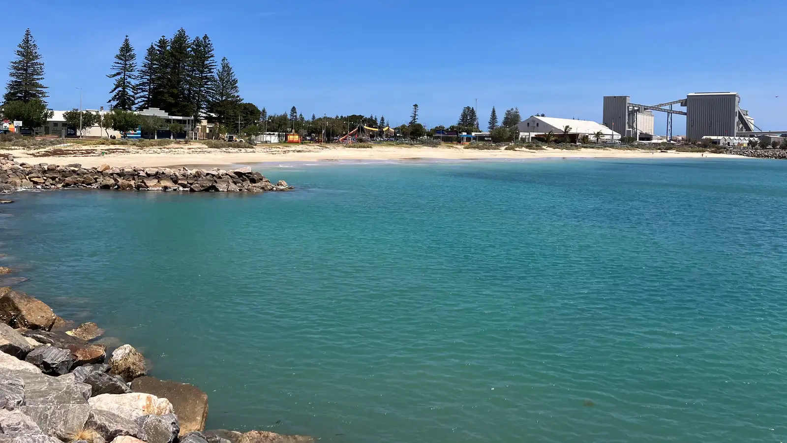 Turquoise water and a sandy foreshore at Geraldton, with Norfolk pines and the port behind