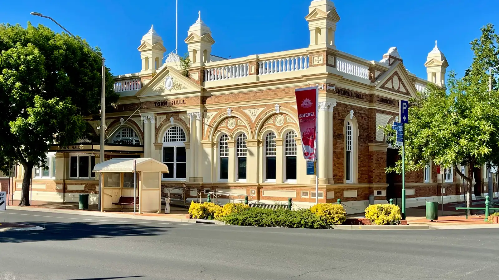 Inverell's ornate heritage Town Hall with flags and garden beds under a clear blue sky
