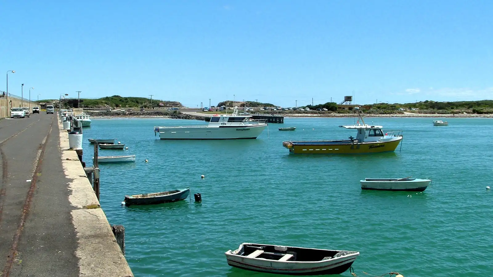 Small boats moored in calm turquoise water along the Warrnambool breakwater under a blue sky